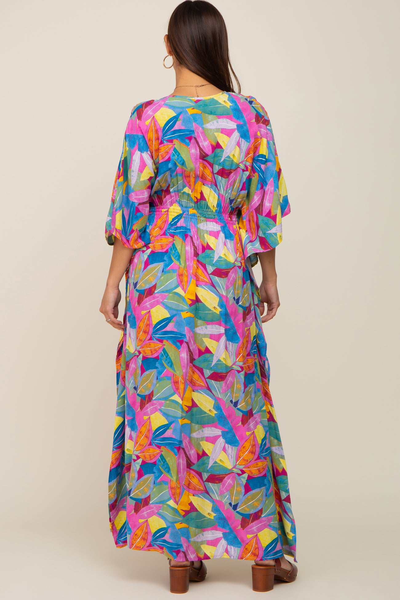 woman wearing a colorful floral-print maternity maxi dress with short flutter sleeves and a cinched waist from the back