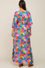 woman wearing a colorful floral-print maternity maxi dress with short flutter sleeves and a cinched waist from the back