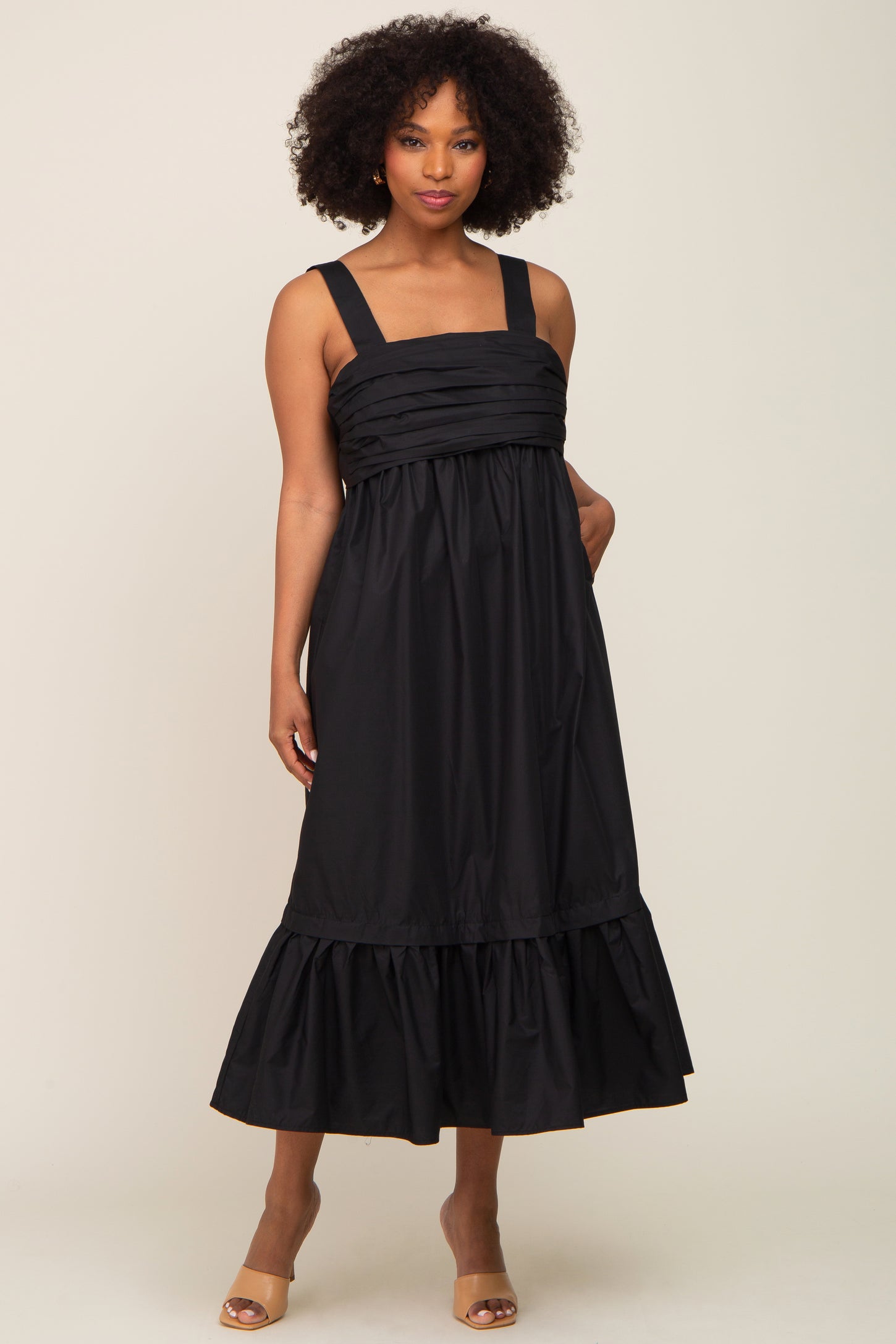 woman with afro hair wearing a black sleeveless midi dress with pleated bodice and ruffled hem