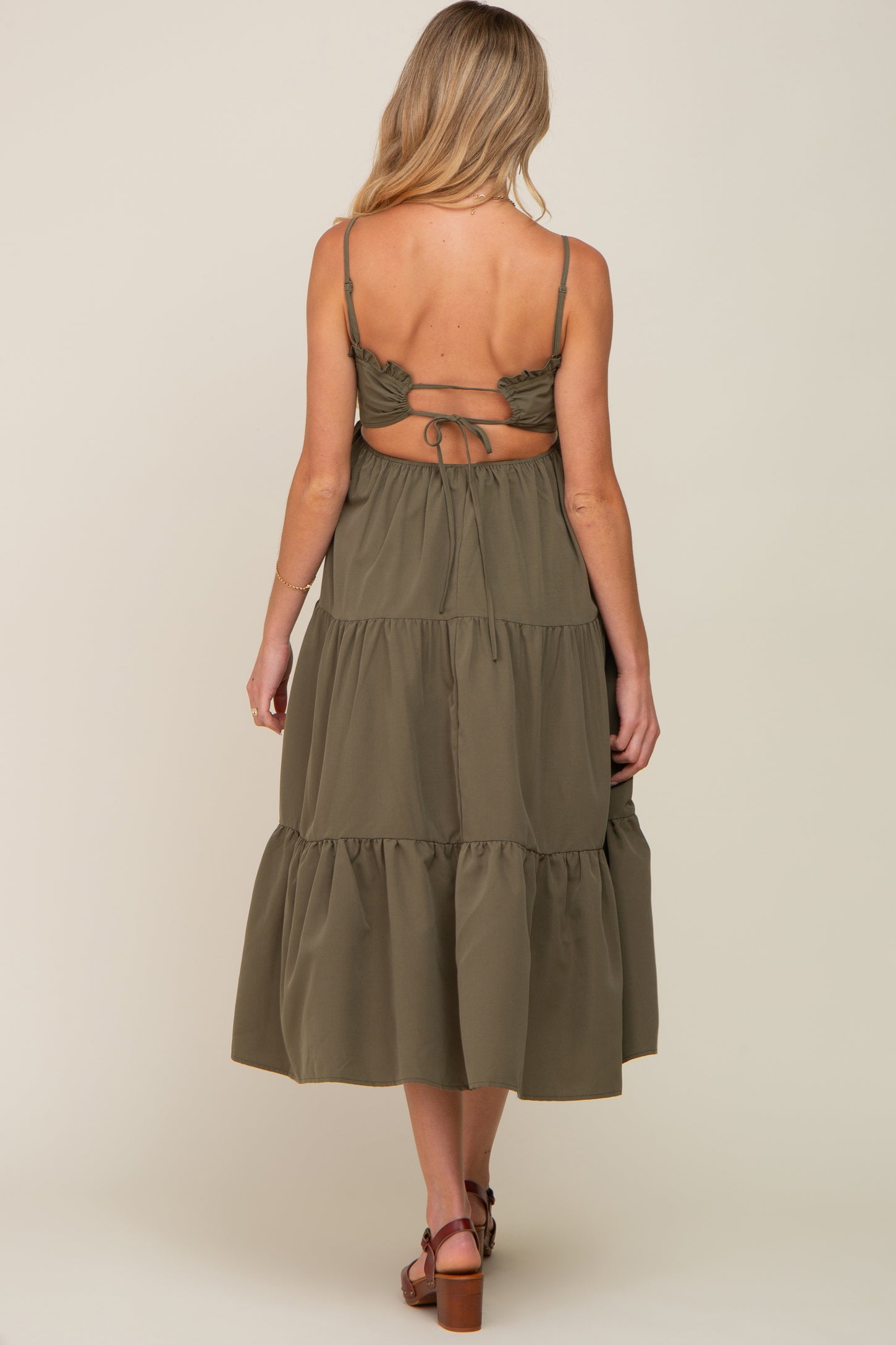 Back view of a woman wearing an olive green tiered midi dress with a tie-back cutout and thin straps