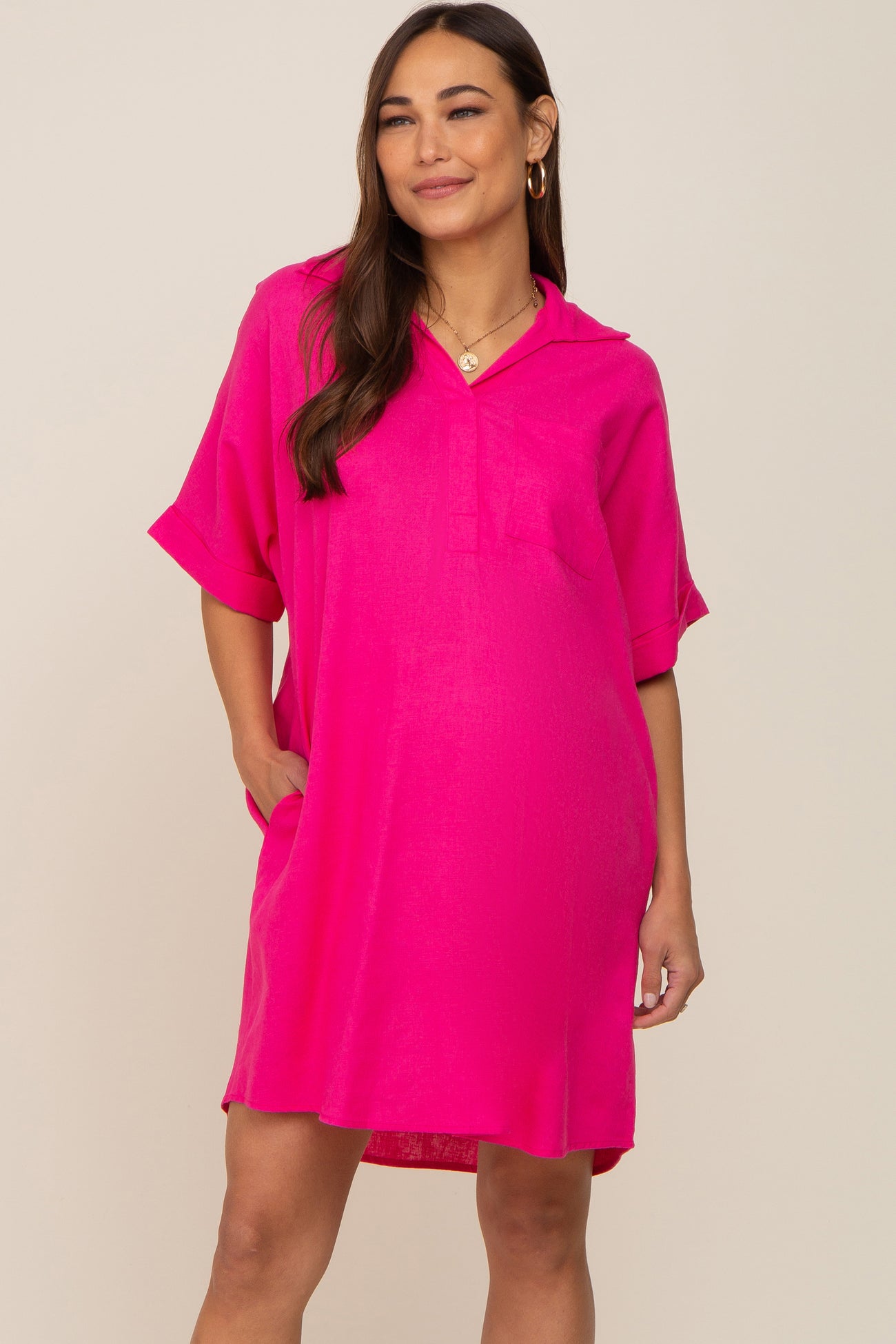Woman wearing a bright pink short-sleeve collared shirt dress with pockets against a neutral background