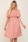 Woman wearing a peach smocked maternity dress with white floral print and flutter sleeves