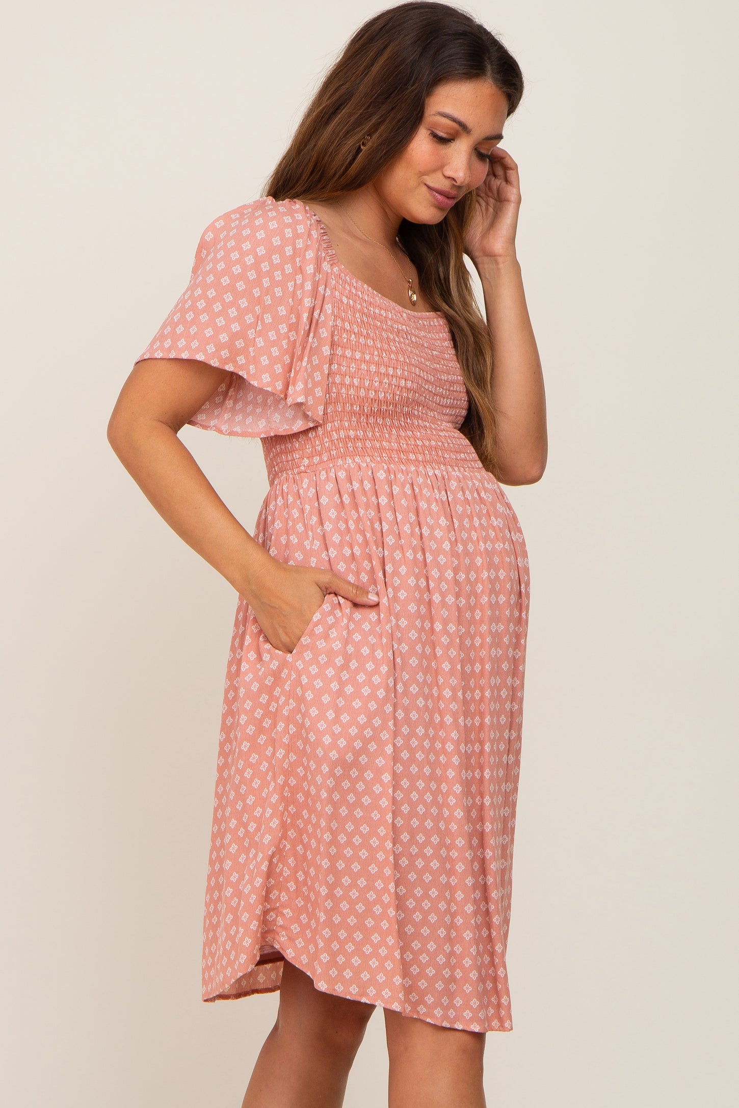 Pregnant woman wearing a pink patterned smocked maternity dress with flutter sleeves and pockets