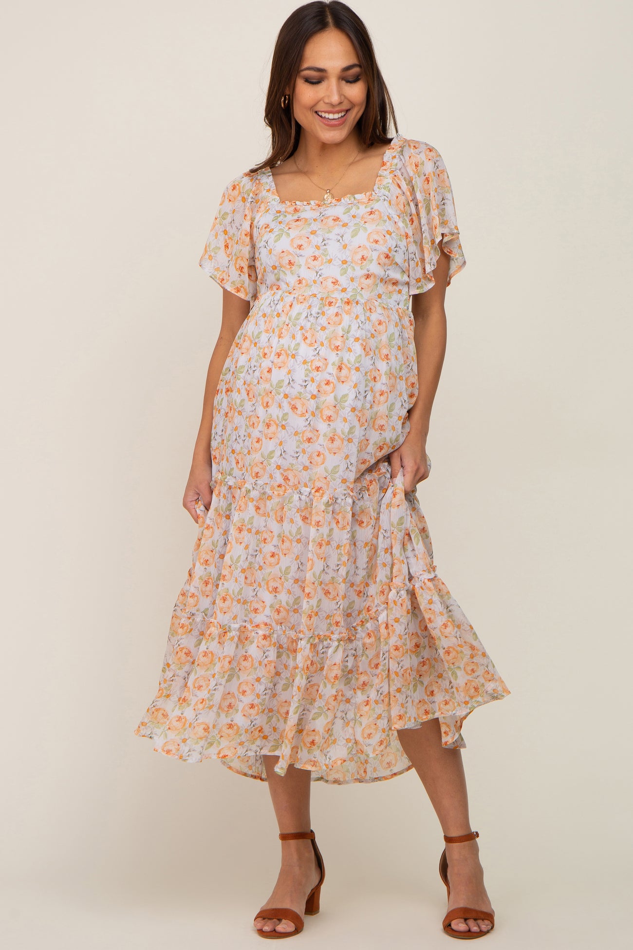 Smiling pregnant woman wearing a floral maternity midi dress with flutter sleeves and tiered skirt