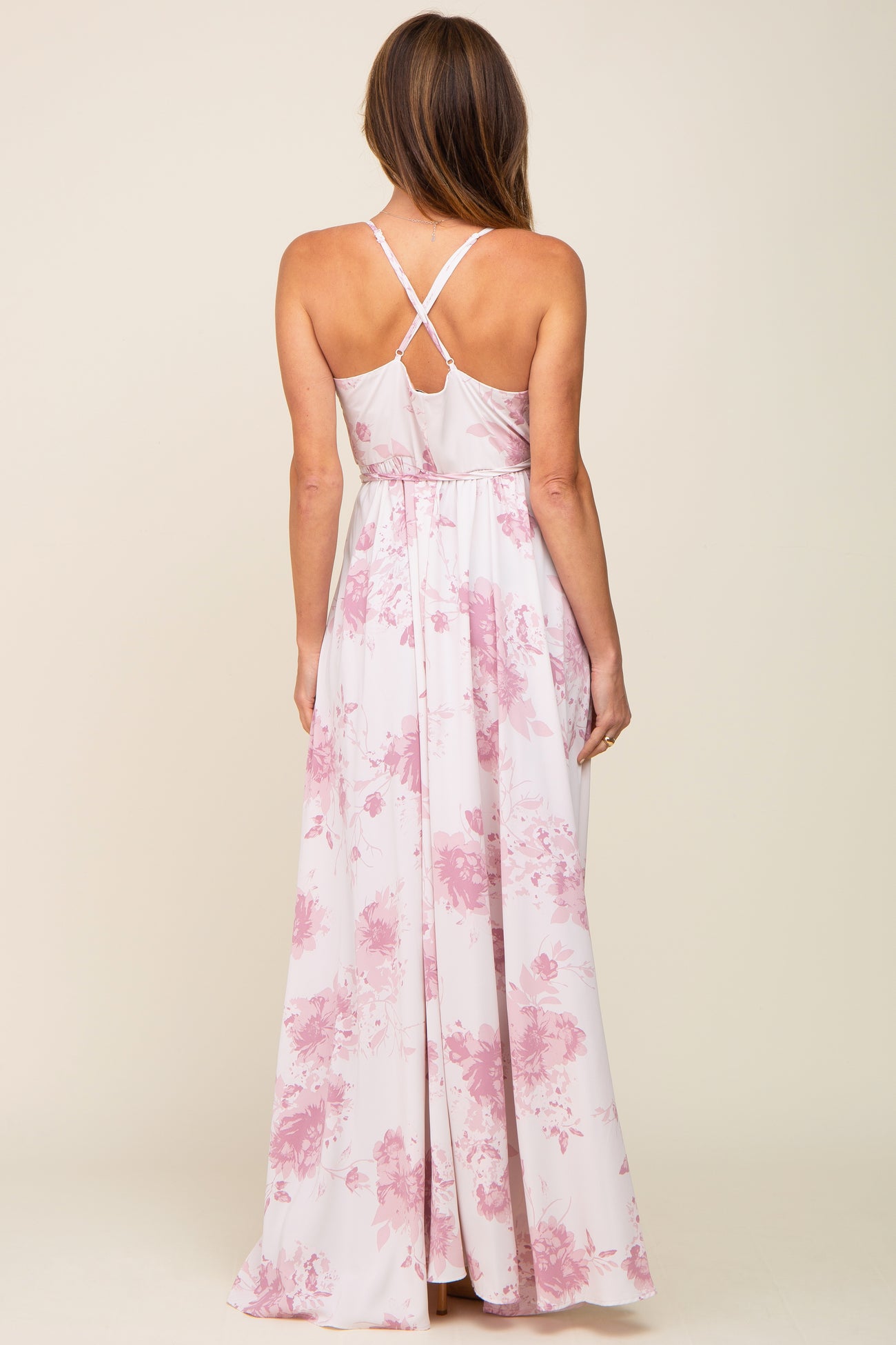 back view of woman wearing light pink floral maxi dress with crisscross straps and tie waist