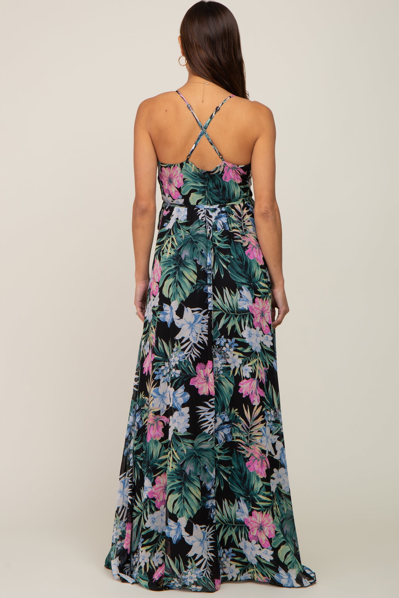 woman wearing a floral print maternity maxi dress with crisscross straps and a flowing design, showing a baby bump
