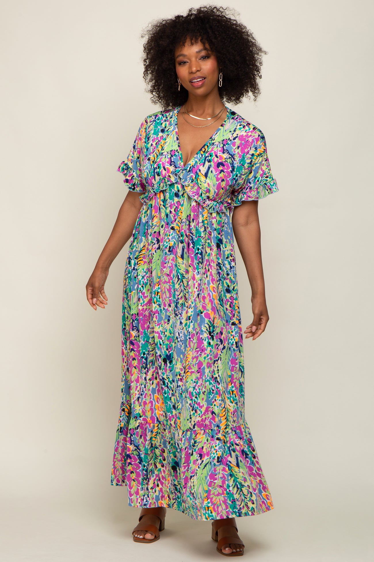 Woman with curly hair wearing a colorful floral print maxi dress with ruffle sleeves and brown sandals