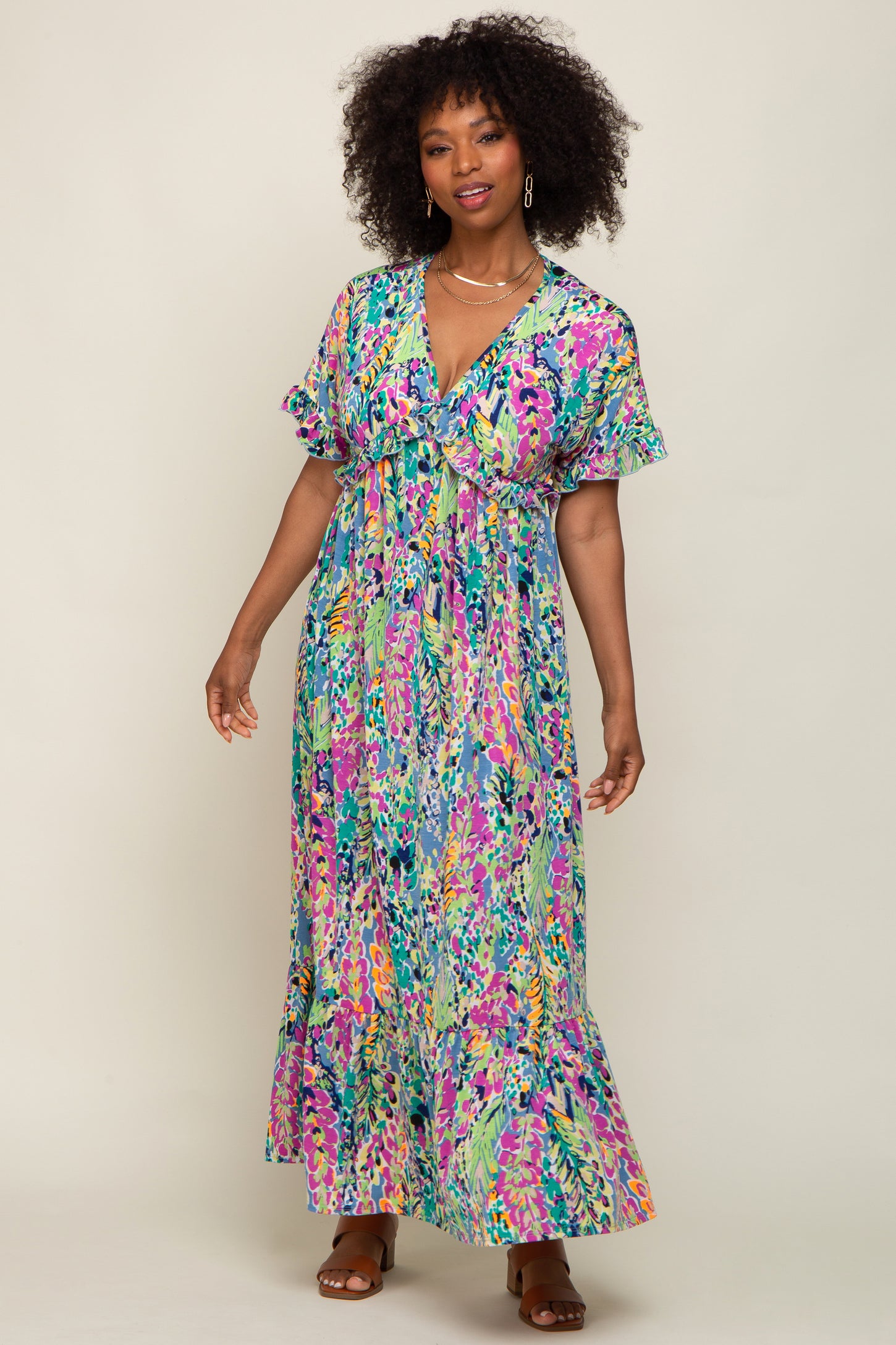 Woman with curly hair wearing a colorful floral print maxi dress with ruffle sleeves and brown sandals
