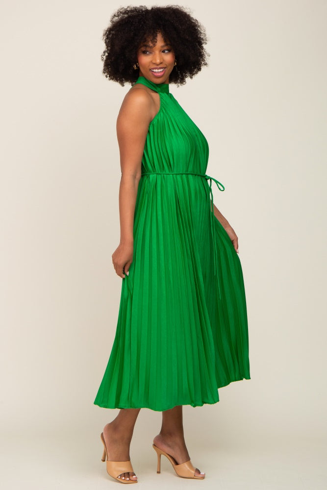 woman with afro hair wearing a green pleated halter midi dress with a waist tie and tan heels