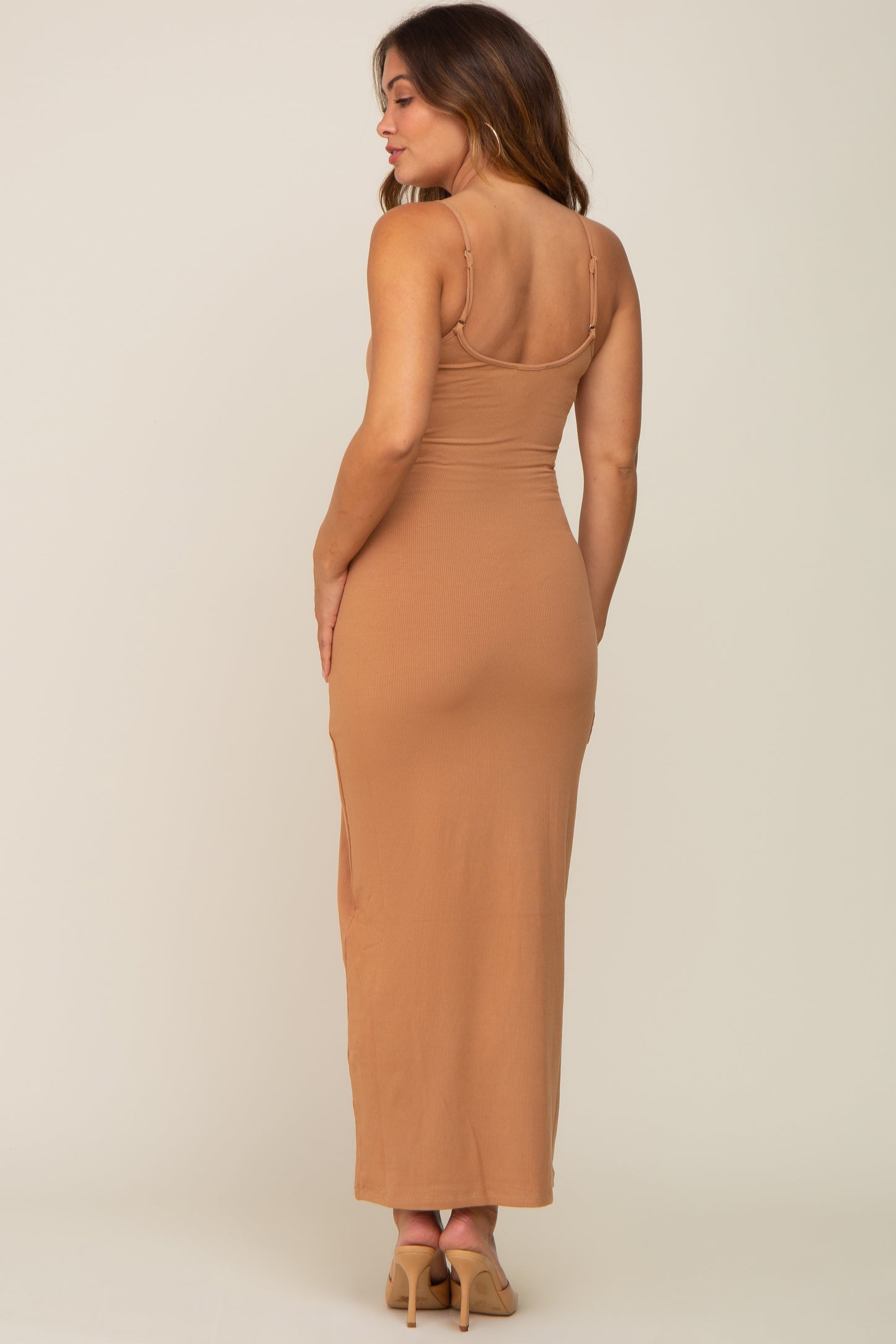 woman wearing a form-fitting tan maternity maxi dress with adjustable straps, showcasing a sleek silhouette from the back