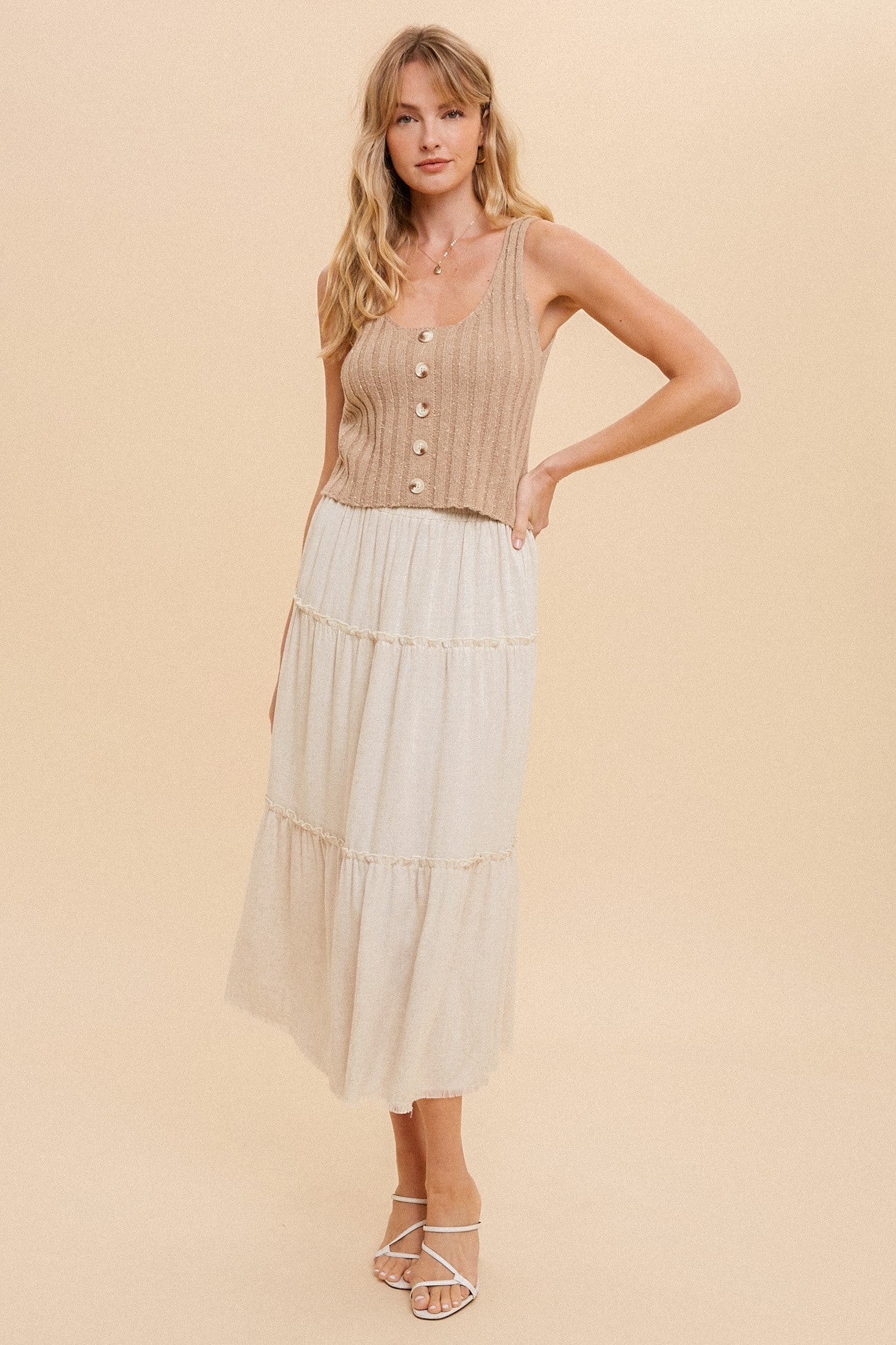 woman wearing a tan ribbed button-front tank top and a cream tiered midi skirt with white strappy sandals