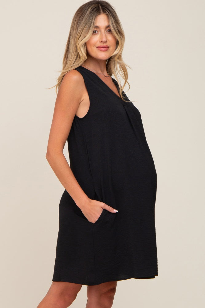 Pregnant woman wearing a sleeveless black maternity dress with pockets against a neutral background