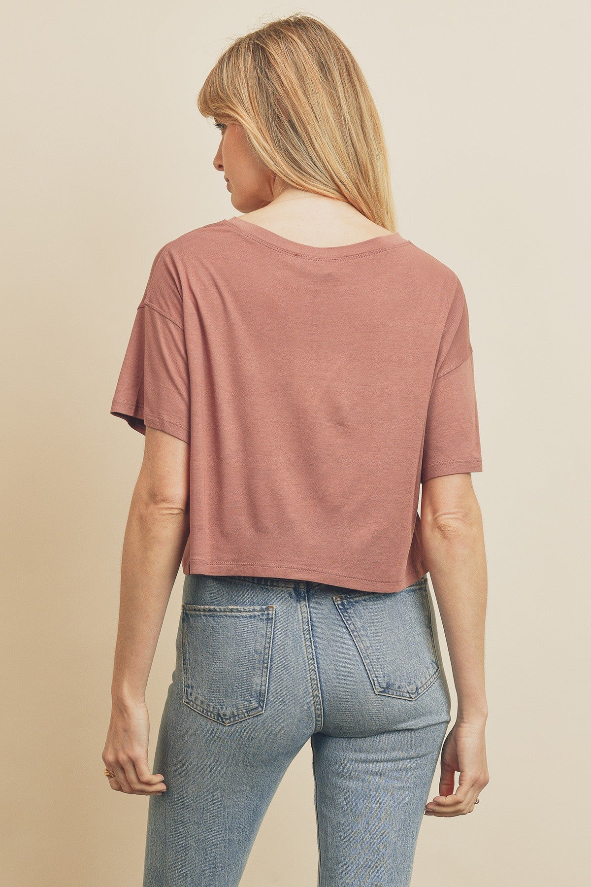 Back view of a woman wearing a dusty rose cropped t-shirt and light wash denim jeans