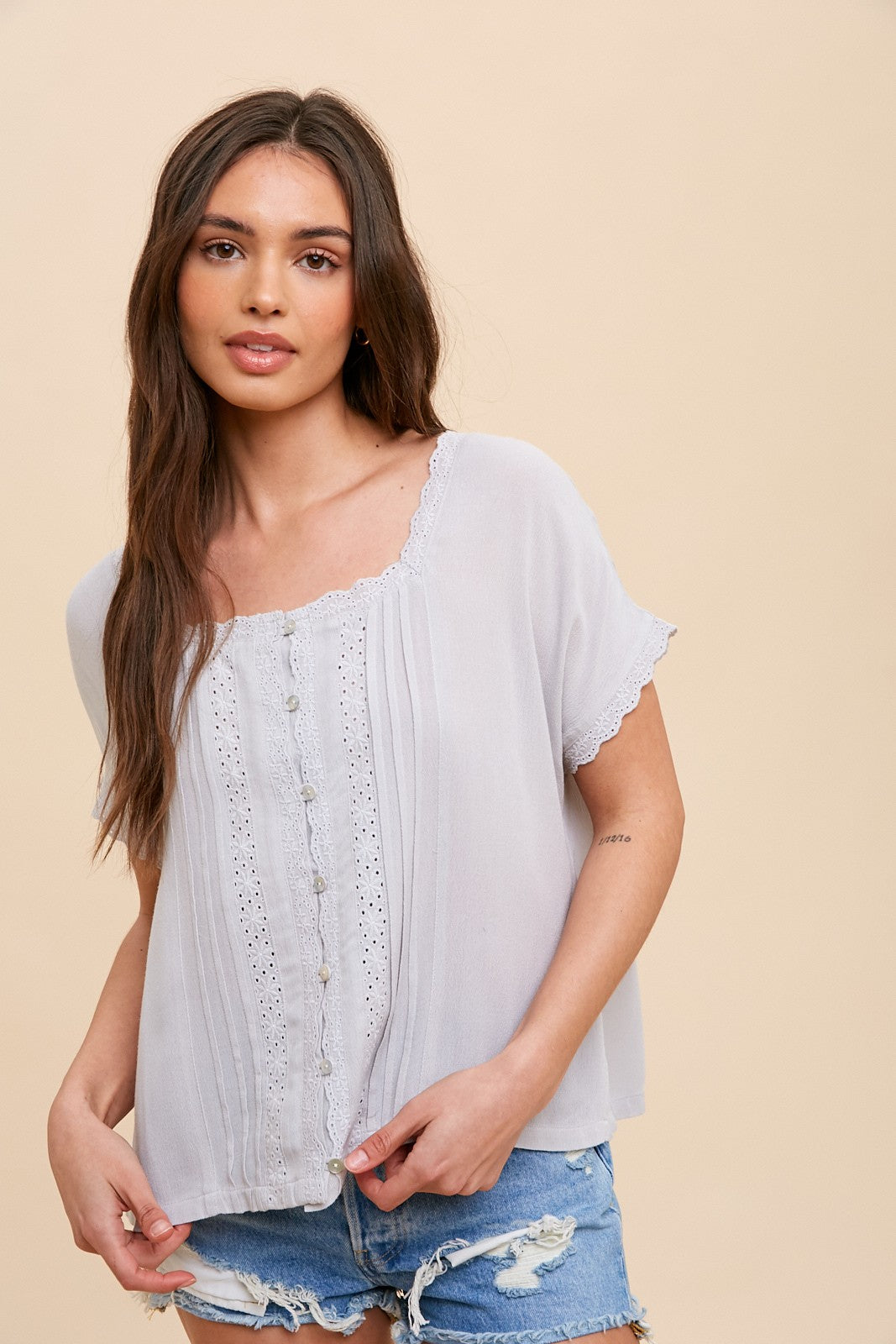 woman wearing a light grey short sleeve button up blouse with lace trim and denim shorts