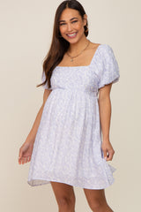 Smiling woman wearing a light blue and white floral maternity dress with puff sleeves and a square neckline