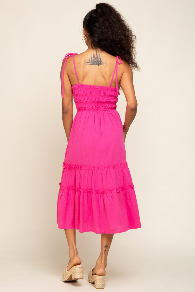 Back view of a woman wearing a hot pink tiered midi dress with smocked bodice and tie straps
