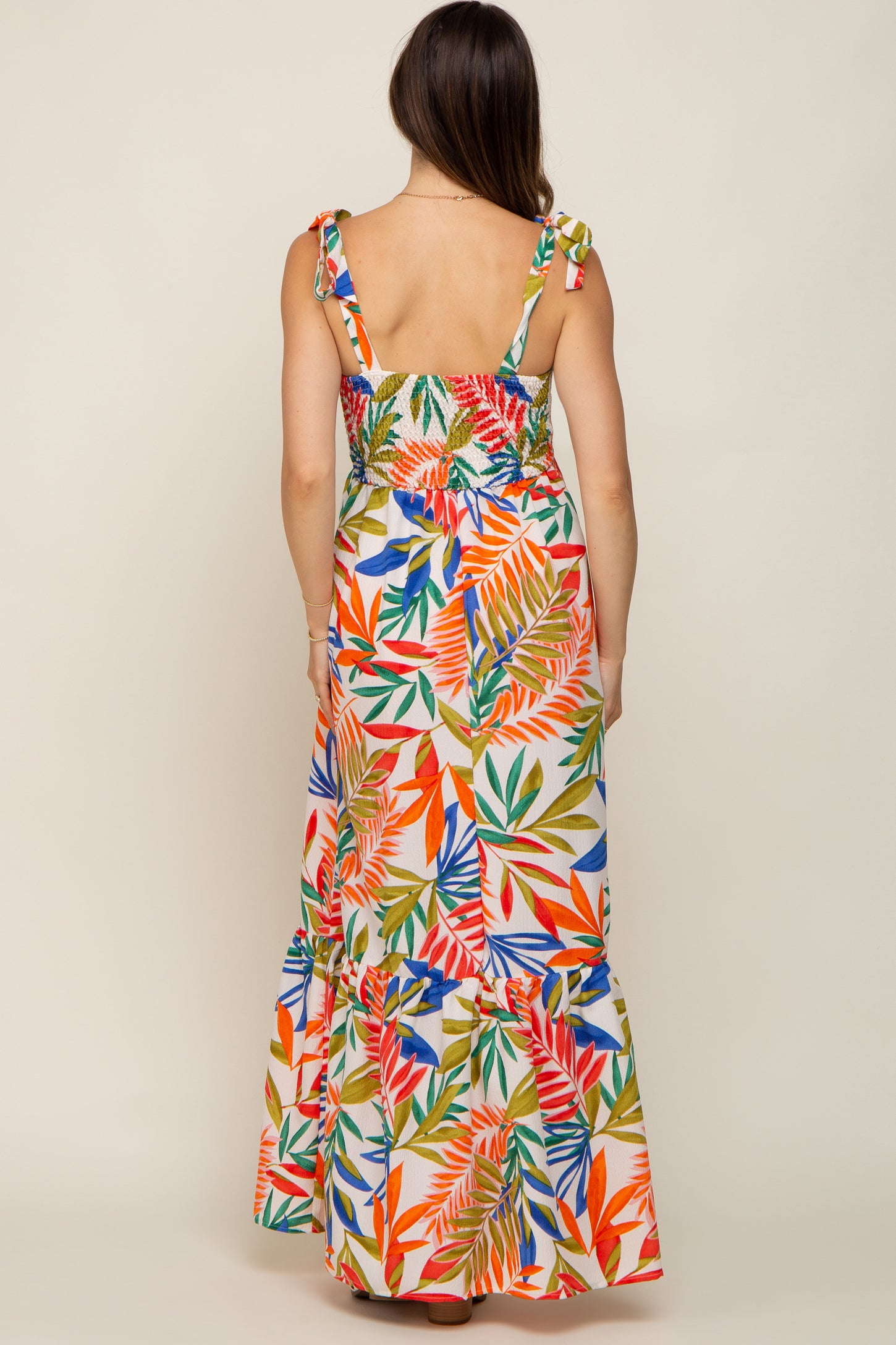 woman wearing a colorful floral print maternity maxi dress with ruffled hem and tie straps, showing her back