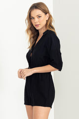woman with blonde hair wearing a black short sleeve romper with a collar and pockets