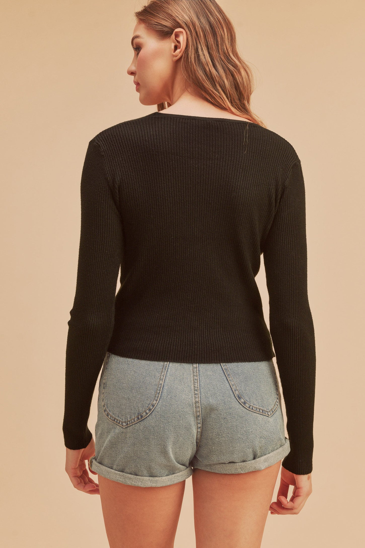 Back view of a woman wearing a black long sleeve ribbed knit top and light wash denim shorts