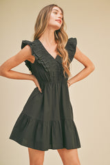 Woman wearing a black sleeveless ruffle mini dress with a v-neckline and tiered skirt