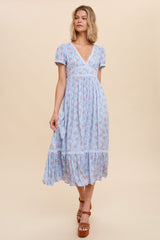 Woman wearing a light blue floral midi dress with lace trim and puff sleeves against a neutral background