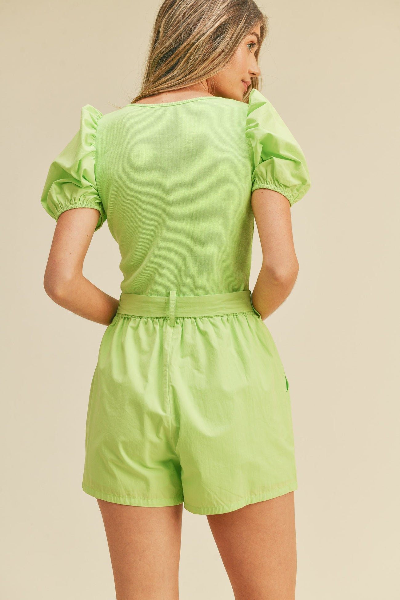Back view of a woman wearing a lime green puff sleeve top and matching high-waisted shorts
