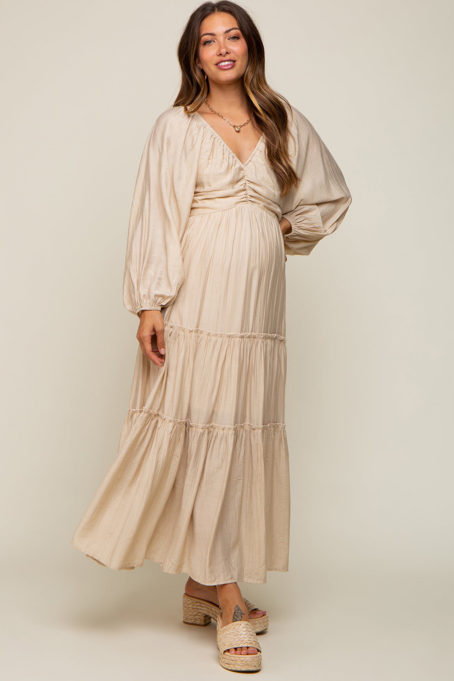 Pregnant woman wearing a beige long sleeve tiered maternity maxi dress with platform sandals