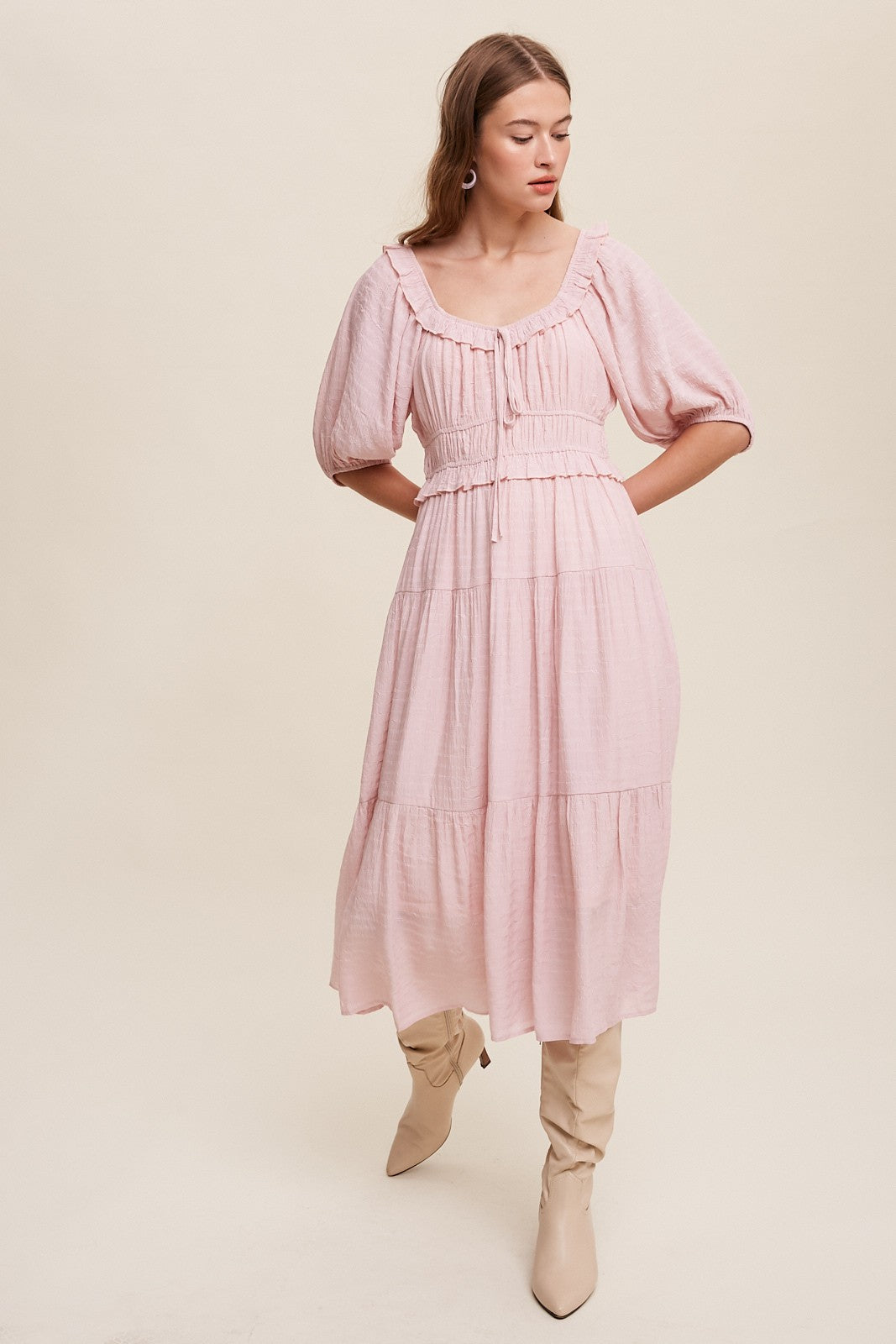 Woman wearing a light pink midi dress with puff sleeves and tiered skirt paired with beige knee-high boots