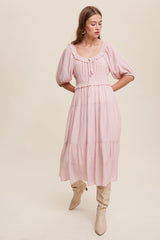 Woman wearing a light pink midi dress with puff sleeves and tiered skirt paired with beige knee-high boots