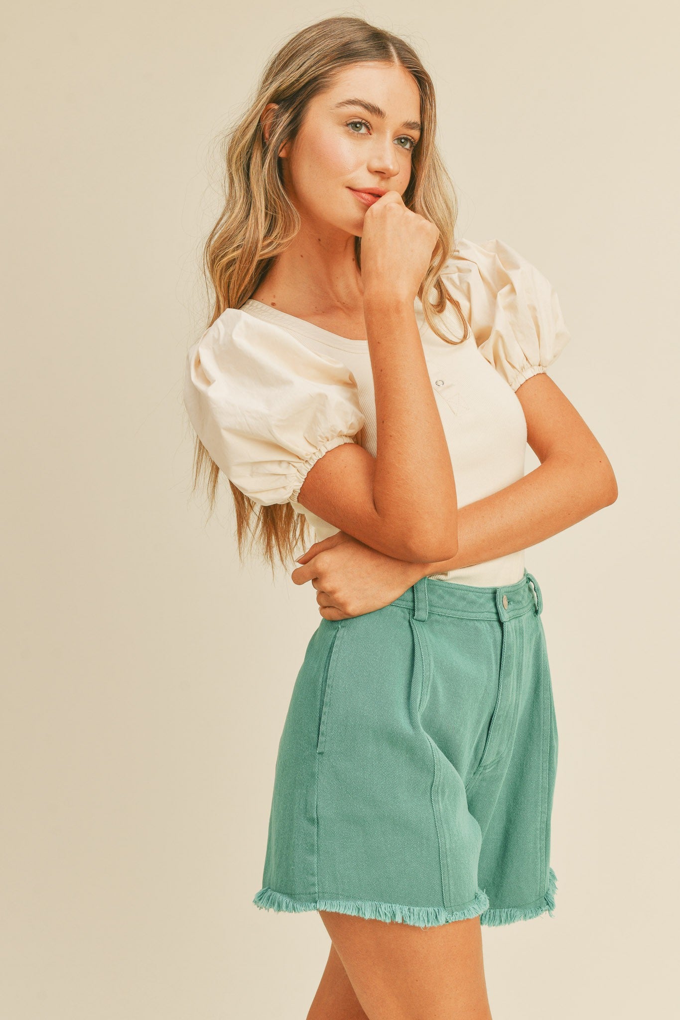 woman wearing cream puff sleeve top and green denim shorts with frayed hem