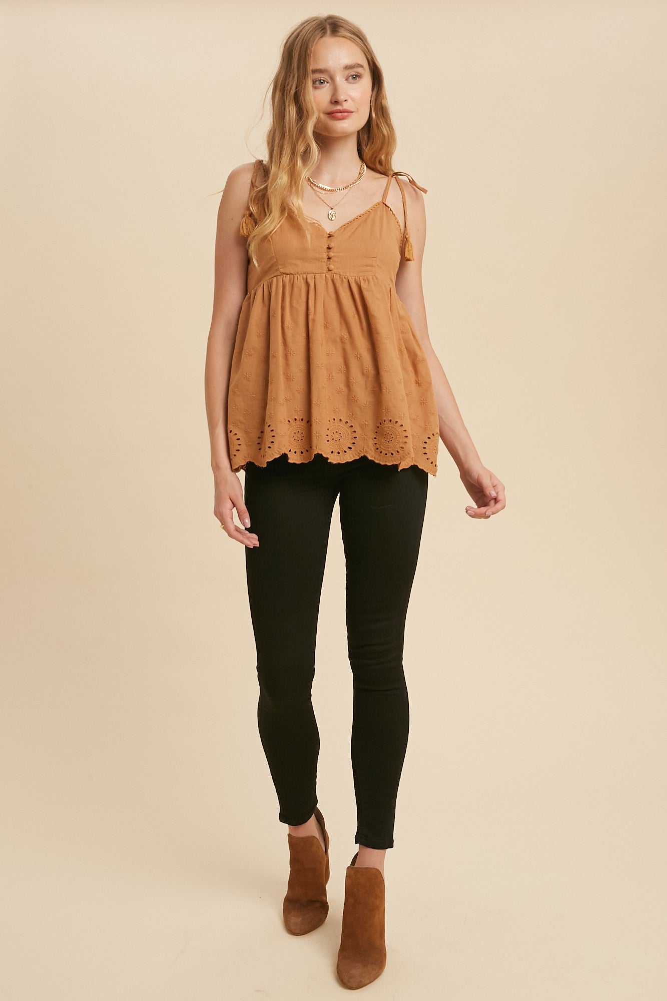 woman wearing a tan eyelet babydoll tank top with black skinny jeans and brown suede ankle boots