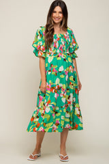 woman wearing a vibrant green floral maternity dress with puff sleeves and a tiered skirt, showcasing a baby bump