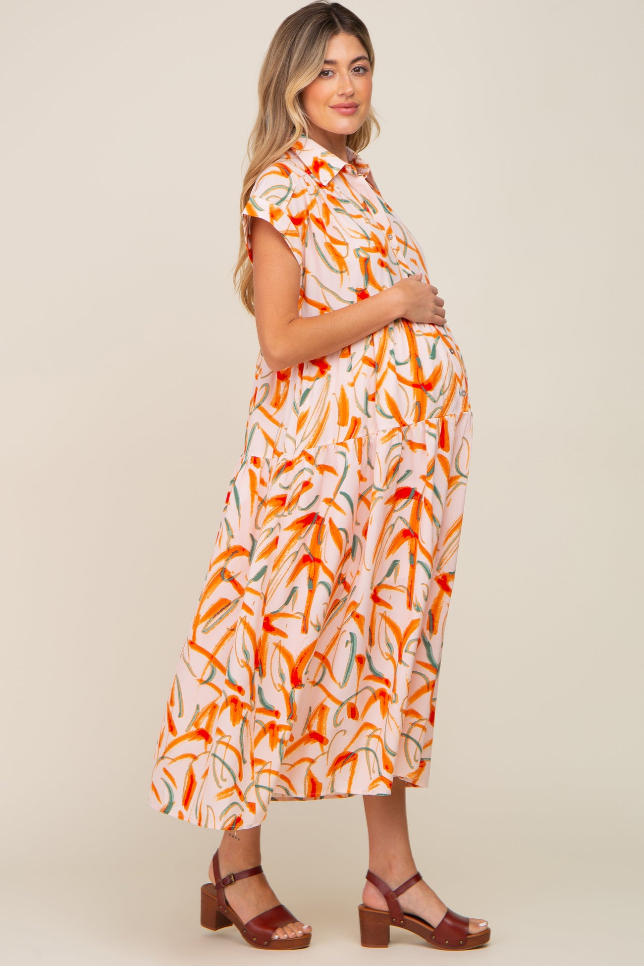 Pregnant woman wearing a pink and orange abstract print maternity midi dress with brown sandals
