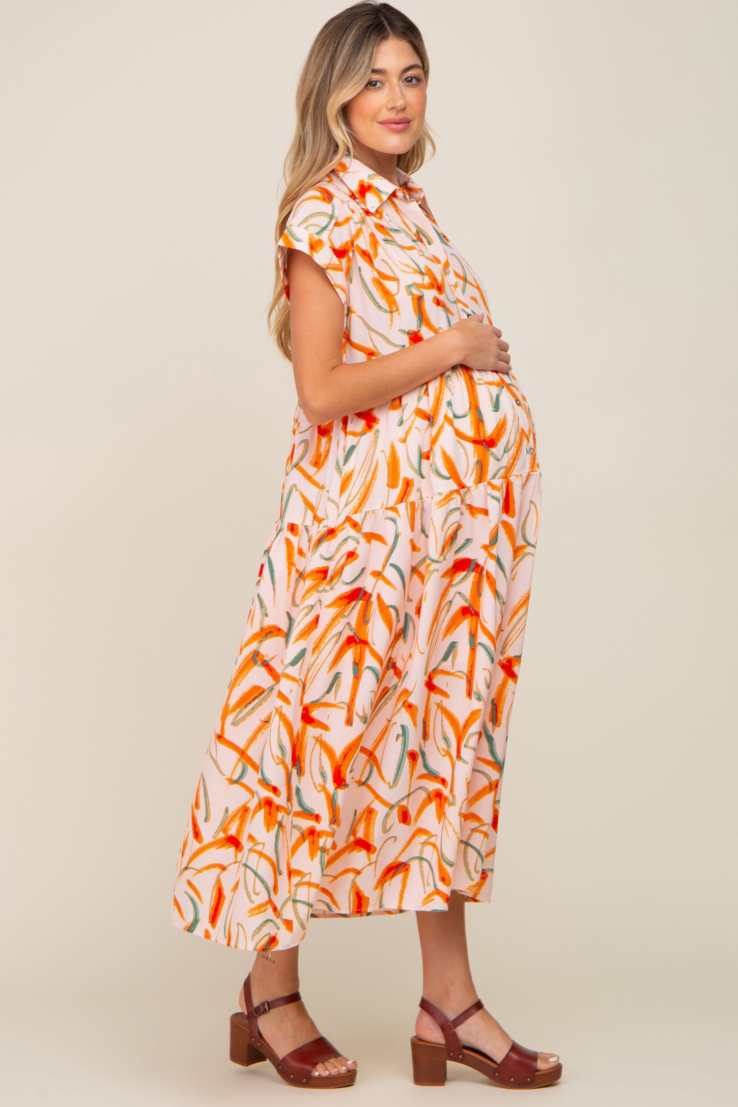 Pregnant woman wearing a pink and orange abstract print maternity midi dress with brown sandals