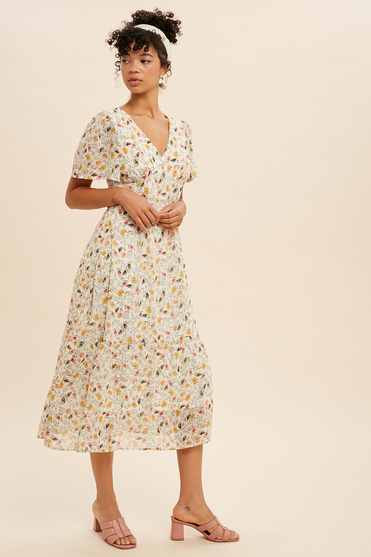 woman wearing a white floral midi dress with short flutter sleeves and pink block heel sandals