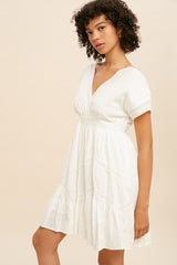 Woman with curly hair wearing a white v-neck mini dress with lace trim and tiered skirt