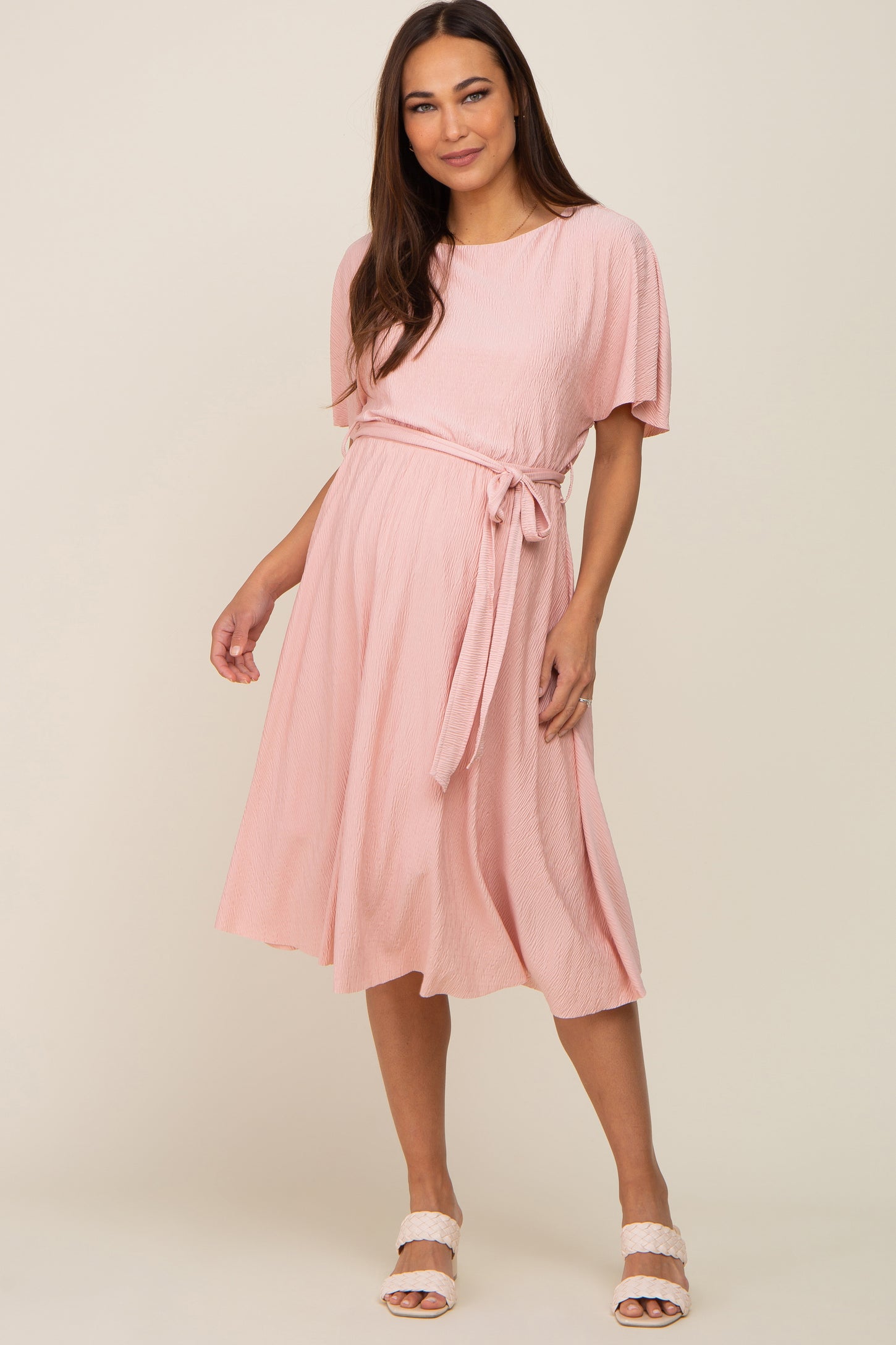 woman wearing a light pink short sleeve maternity midi dress with a waist tie and pleated texture