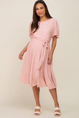 woman wearing a light pink short sleeve maternity midi dress with a waist tie and pleated texture