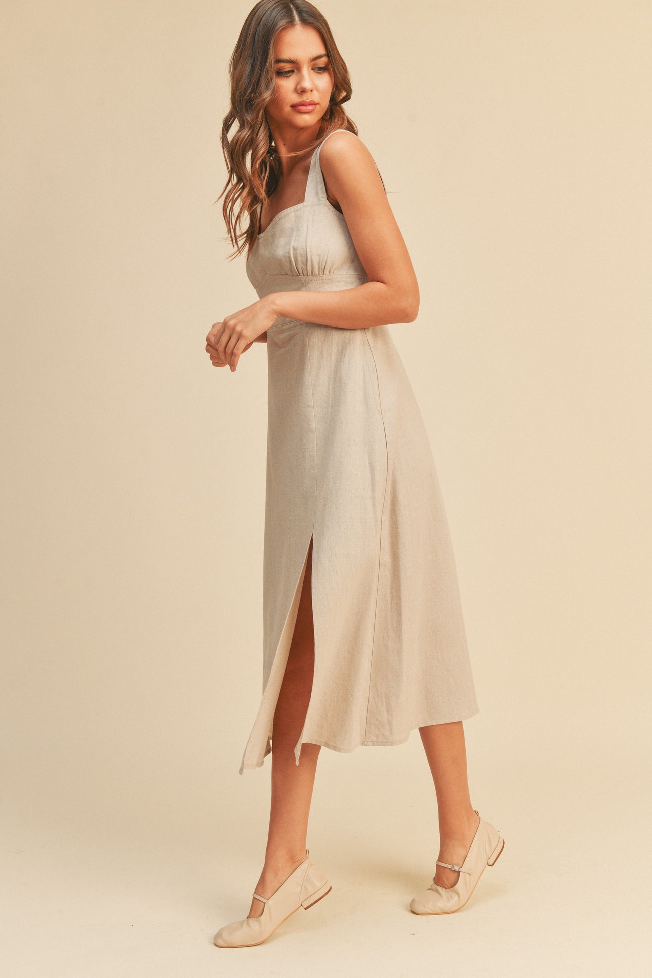 woman wearing a beige linen midi dress with a side slit and matching flat shoes