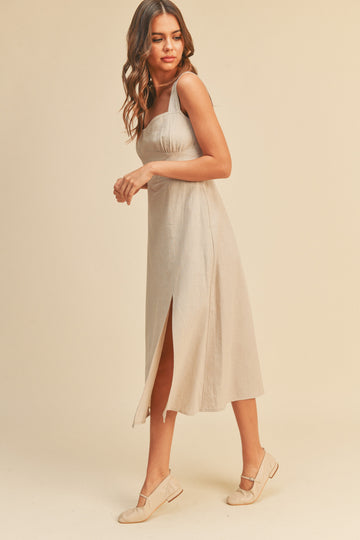 woman wearing a beige linen midi dress with a side slit and matching flat shoes