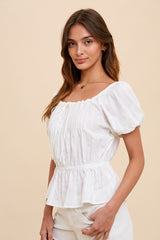 Woman wearing a white puff sleeve peplum top with a square neckline and cinched waist