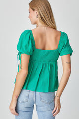 Woman wearing a green puff sleeve smocked top and light wash denim jeans viewed from the back