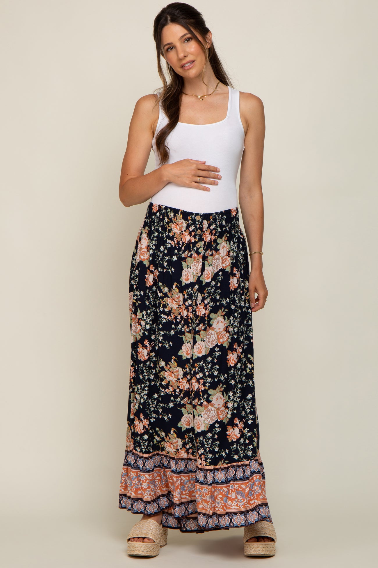 Pregnant woman in white tank top and navy floral maternity maxi skirt with ruffled hem and platform sandals