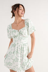 woman wearing a white and green floral puff sleeve mini dress with a square neckline and tie front