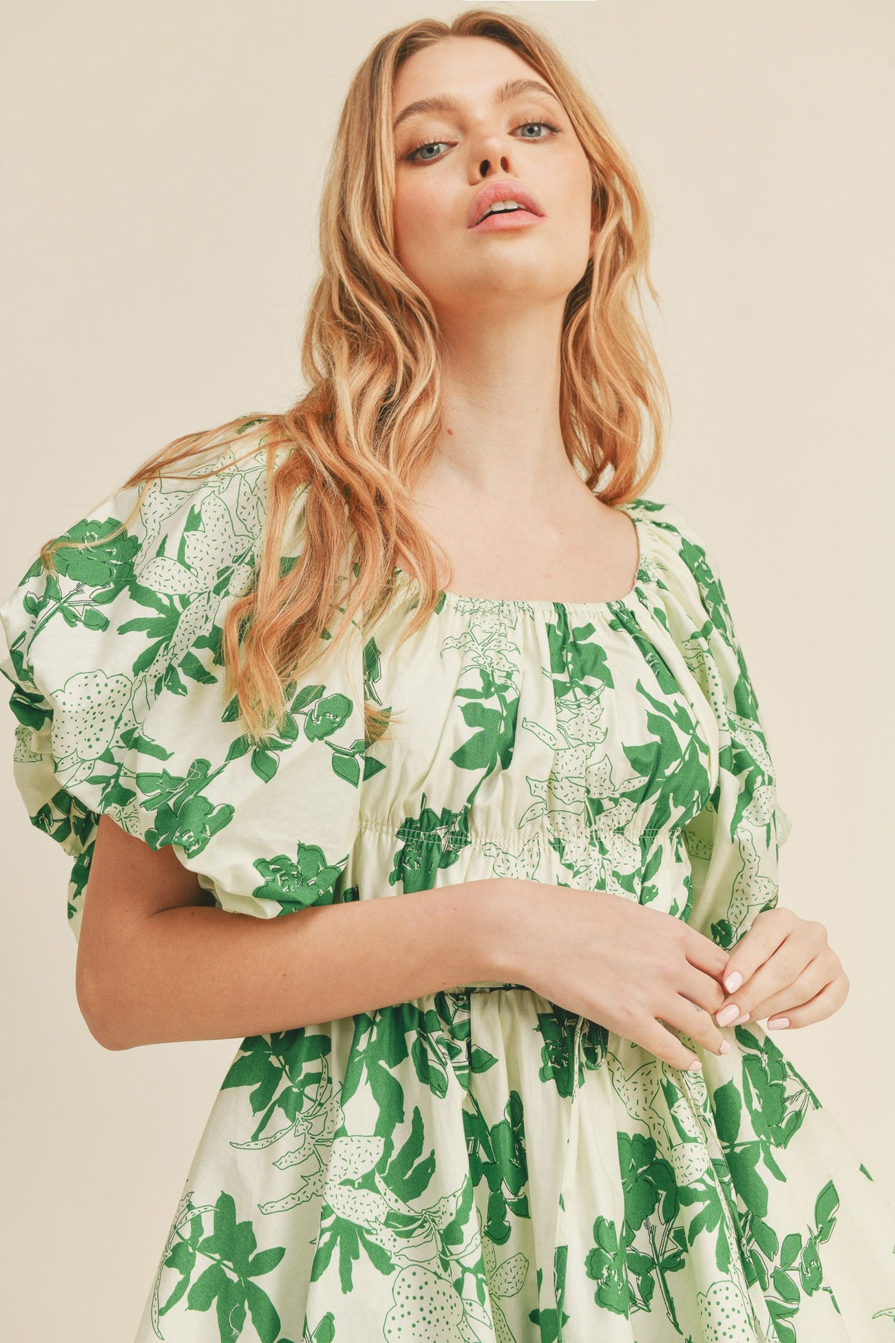 Woman wearing a cream puff sleeve dress with a green floral print and square neckline