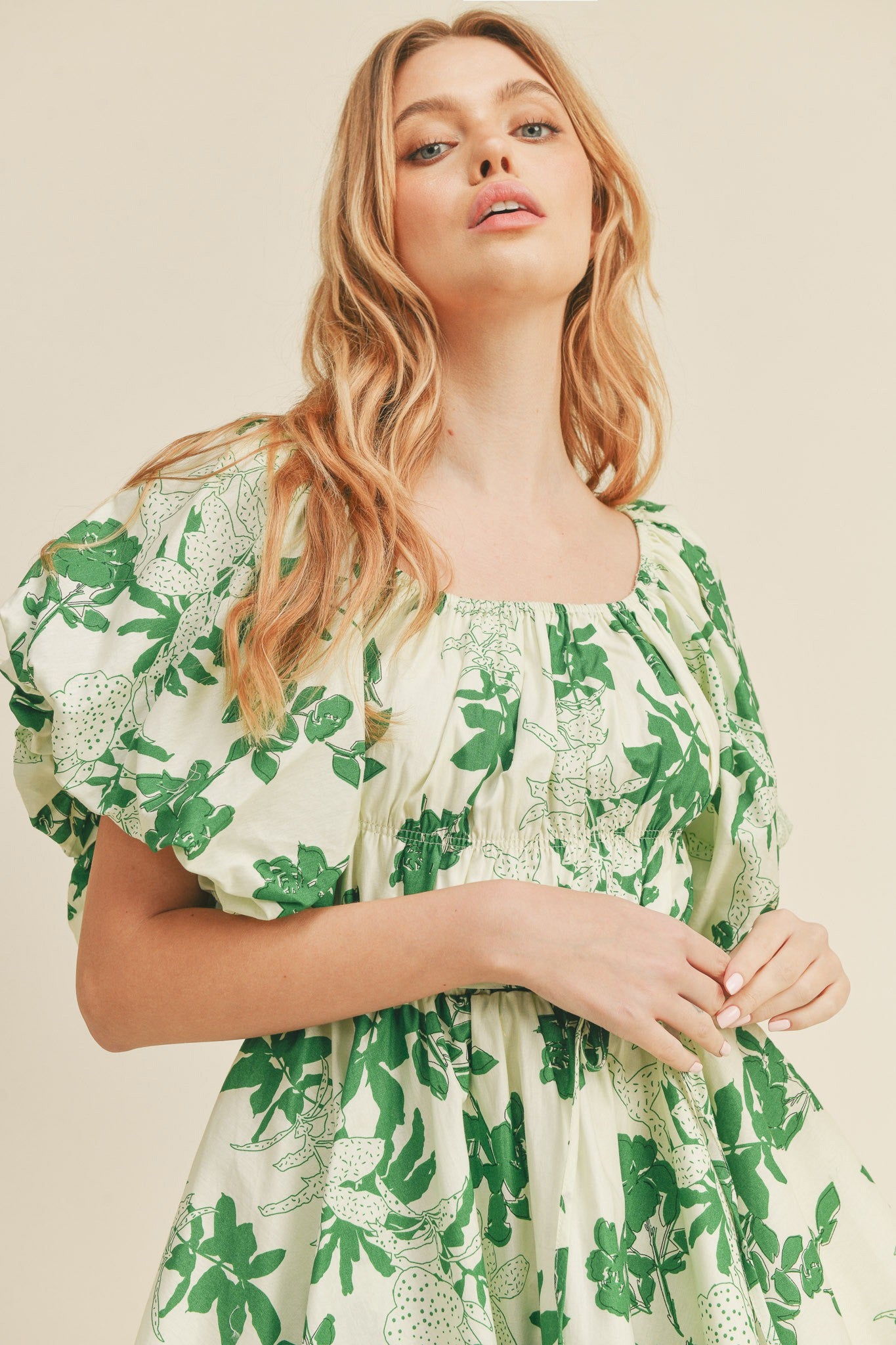 Woman wearing a cream puff sleeve dress with a green floral print and square neckline