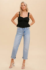 woman wearing a black smocked peplum tank top and light wash straight leg jeans with white strappy heels