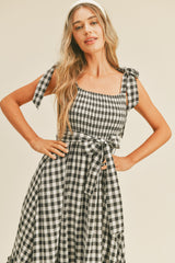 Woman wearing a black and white gingham midi dress with tie straps and a matching waist bow