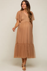 woman wearing a tan maternity dress with short flutter sleeves and a tiered tulle skirt, showcasing her baby bump
