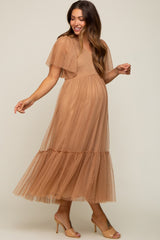 woman wearing a tan maternity dress with flutter sleeves and a tiered tulle skirt, showing her baby bump